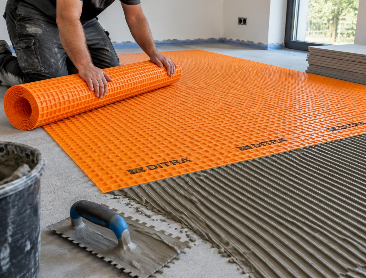 Orange uncoupling membrane being rolled out over adhesive on a screed floor